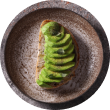 A minimalist top-down view of Voro Food's Avocado Toast, featuring artfully fanned avocado on a rustic stone plate.